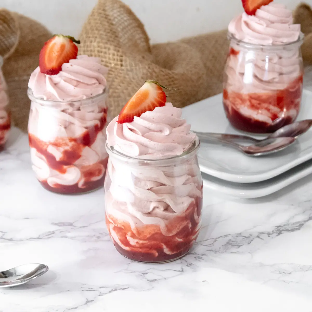 Vegan white chocolate and strawberry mousse pipped into jars that are resting on plates.