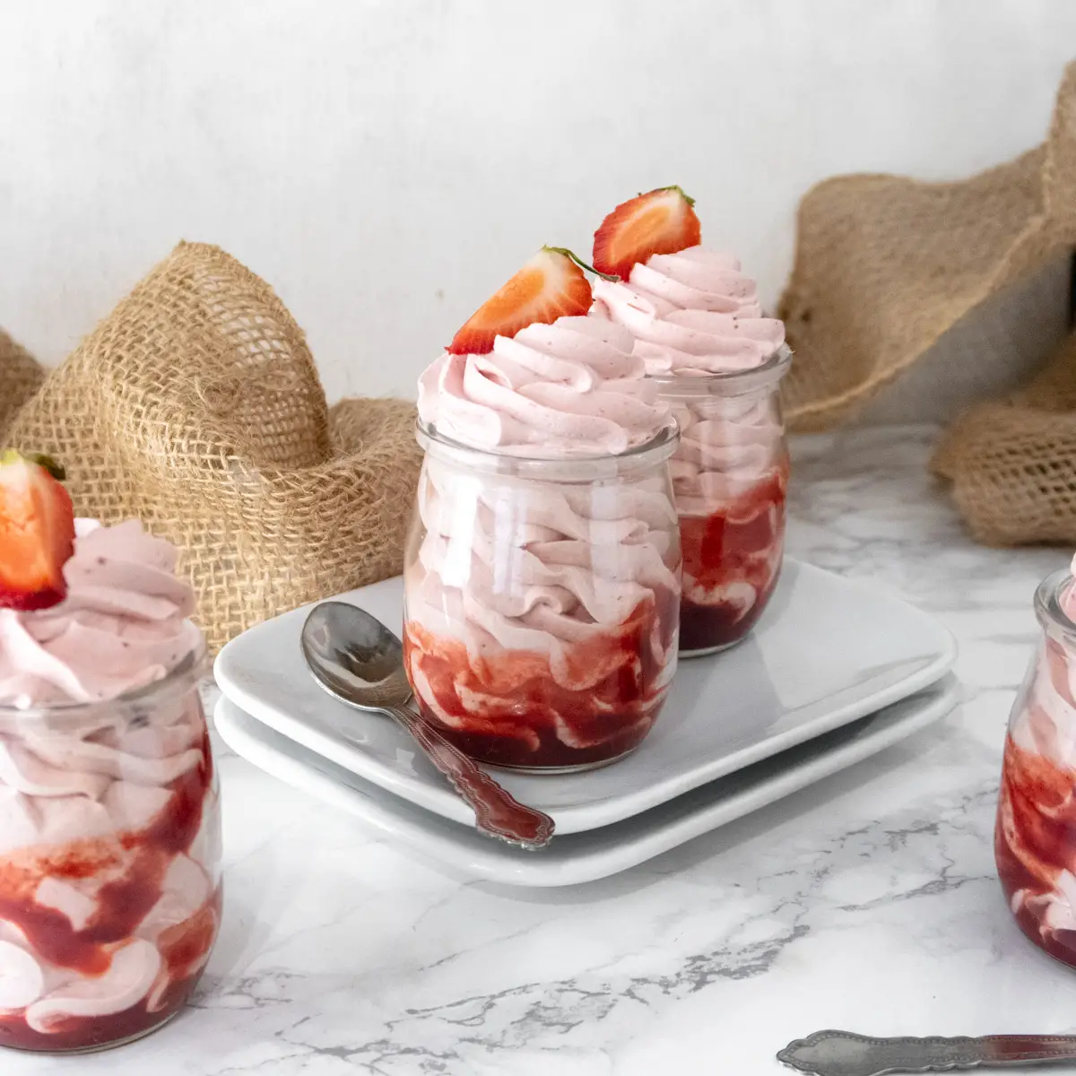 Vegan white chocolate and strawberry mousse pipped into jars that are resting on plates.