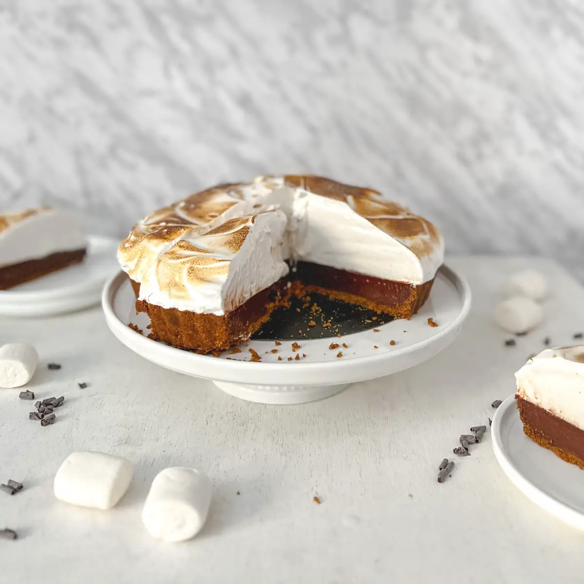 A vegan s'more tart with a piece missing to show the inside of the tart sitting on a cake stand.