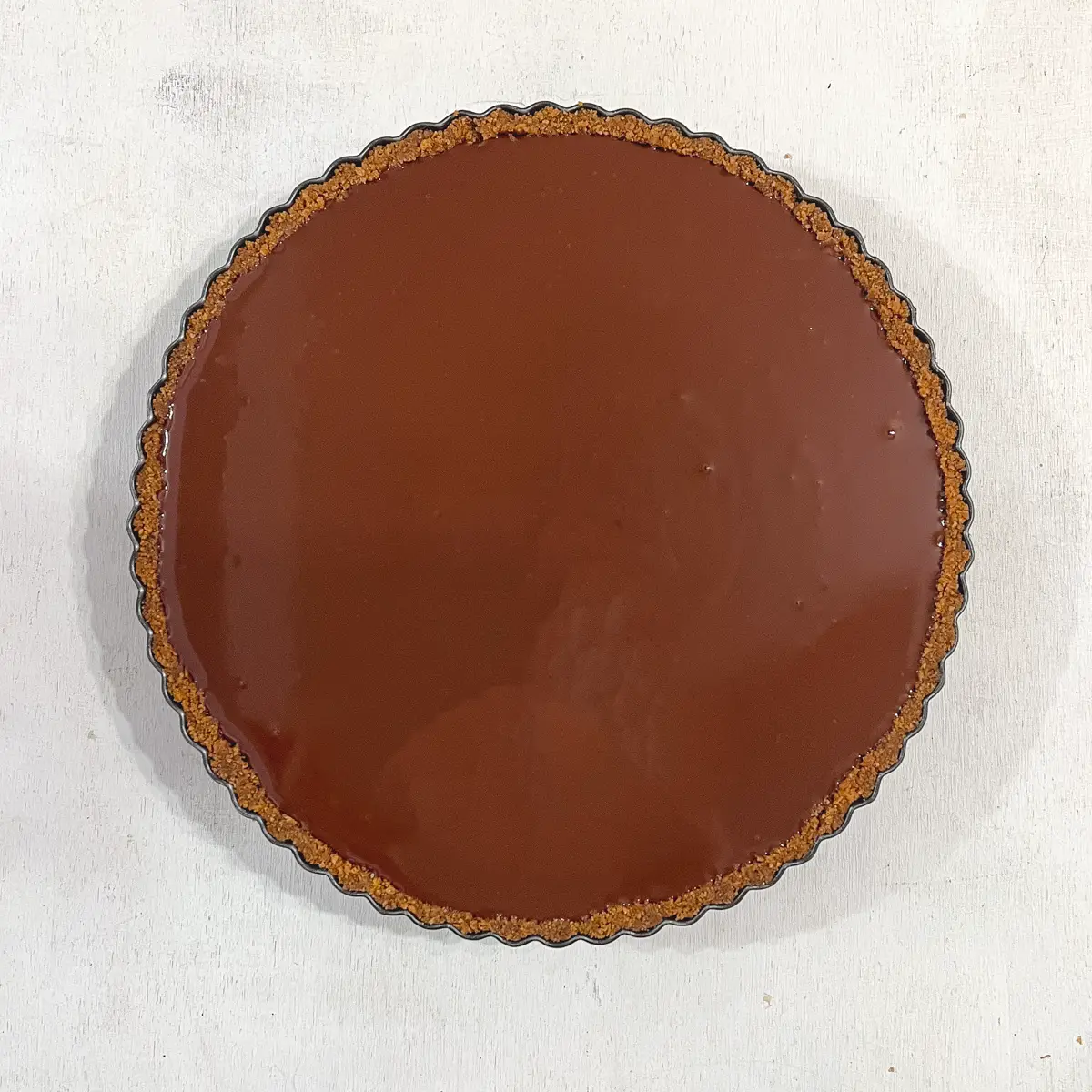 A vegan cookie crust tart filled with glossy chocolate ganache.