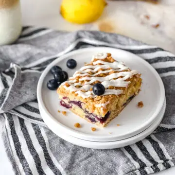 A piece of vegan blueberry coffee cake on a palte sitting on top of a stripped dishtowel.